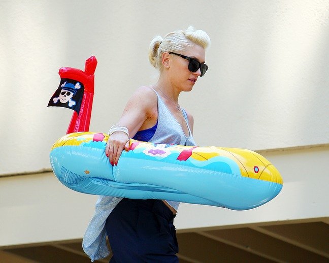 Gwen Stefani white tank top, blue pants cuffed, childs pool toy, sunglasses