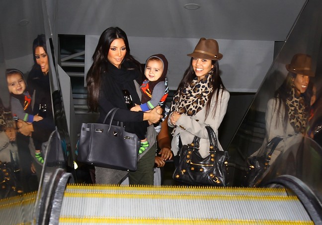 Kourtney Kardashian, Kim Kardashian, animal print scarf, brown hat, black tote bags, black sweater, airport