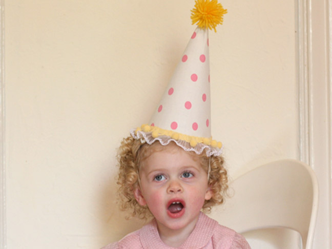 a smiling child with the homemade party hat on her head