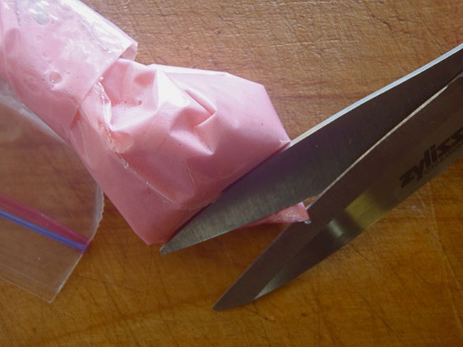 pink meringue in a ziploc bag being cut with kitchen shears