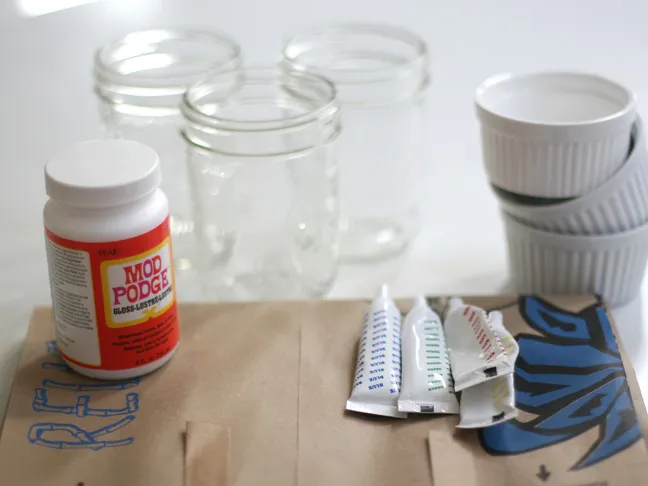 a bottle of mod podge shown with assorted food coloring tubes and empty ramekins in the background