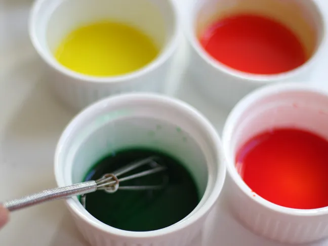 4 ramekins each being whisked with yellow, green, red and blue food coloring
