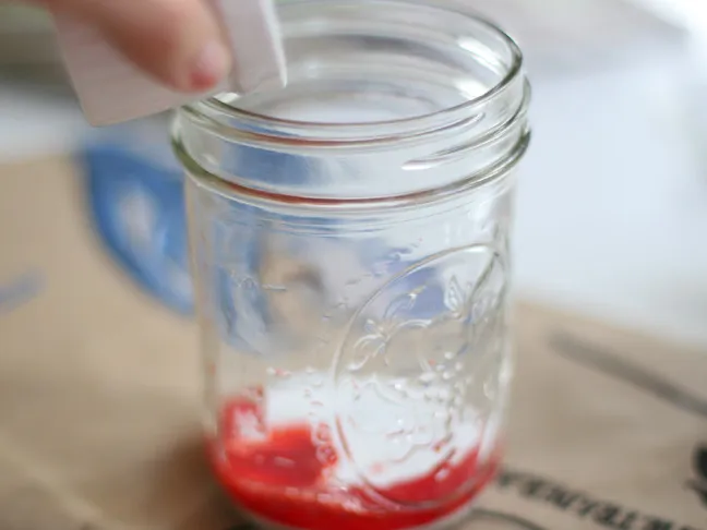 red food coloring being poured in to a mason jar with white mod podge on the bottom