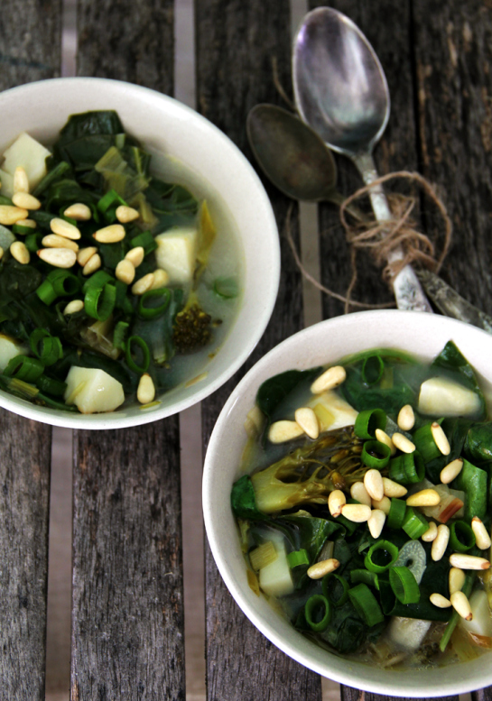 Green Superfood soup in a white bowl topped with pine nuts
