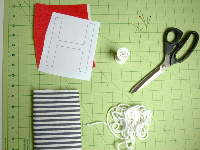 the letter "H" drawn on a piece of paper on top of red felt, pictured with cutting scissors, clothing pins and a cutting board