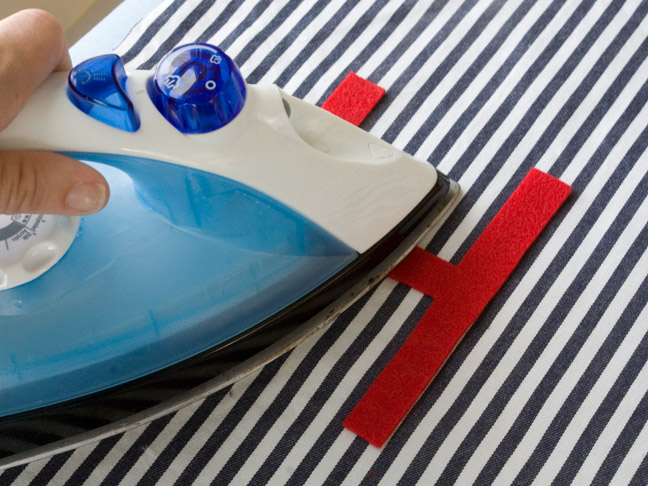 Using a iron over the red felt H to adhere it to the blue and white striped fabric