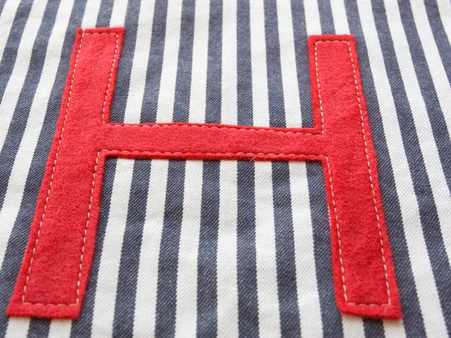 a close up of the "H" sewn on to the white and blue pinstriped fabric