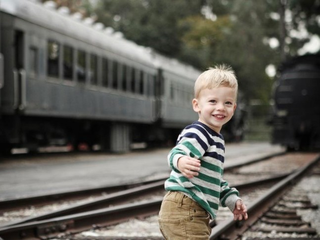 a little blonde boy smiles and runs along the train track