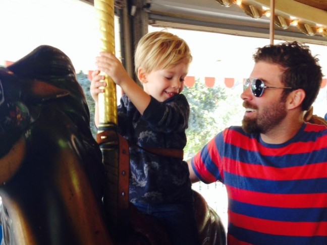 A little boy with his father rides the merry go round