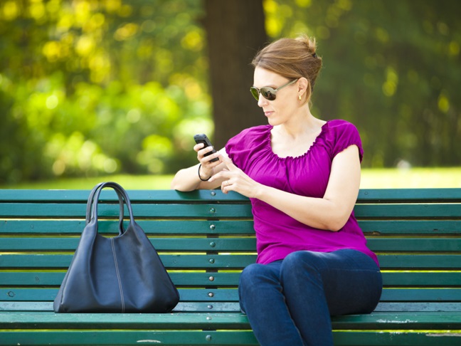 woman texting on park bench