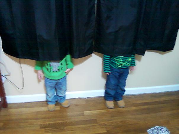 two boys playing hide and seek behind a curtain