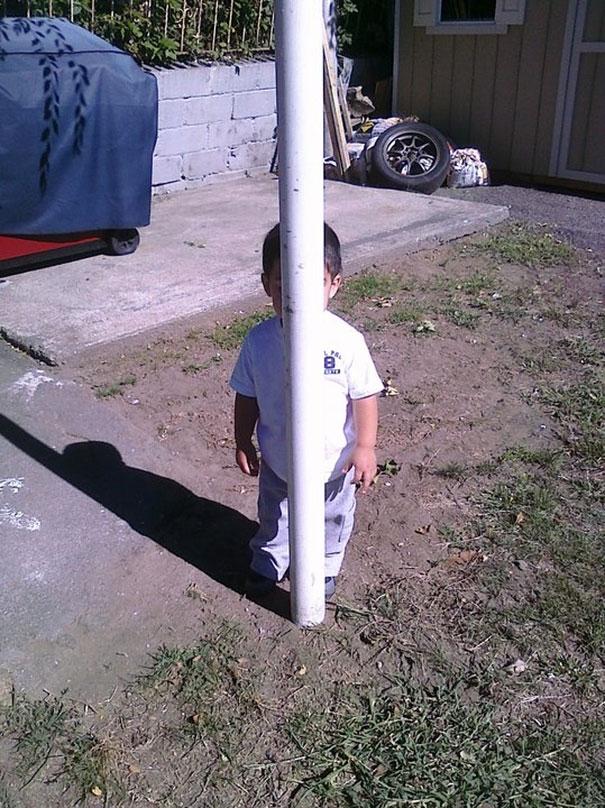 small boy hiding behind a white pole