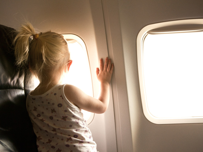 Toddler girl looking out airplane window in flight