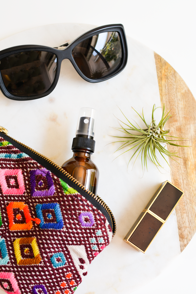 colorful makeup pouch with face mist, sunglasses, lipstick, and air plant