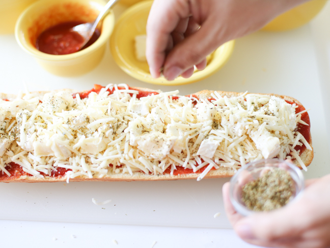 hand sprinkling oregano on pizza bread