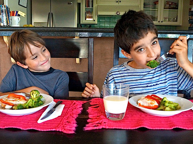 two smiling boys eating broccoli-red placemats