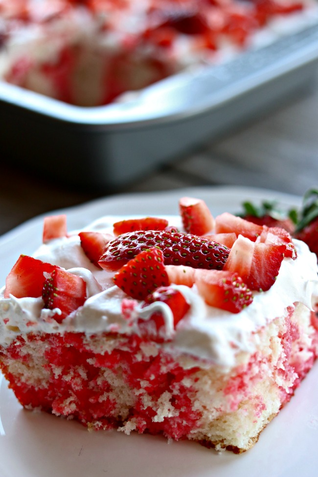 Strawberry Jello Poke Cake--an easy poke cake that starts with a white cake mix, strawberry gelatin is poured into the holes in the cake and then the cake is topped with whipped topping and fresh strawberries. Perfect for potlucks and gatherings!