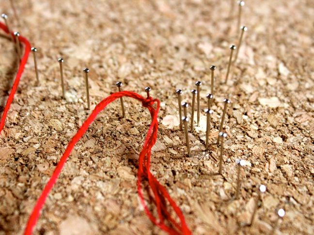 red-string-tied-around-a-pin-pushed-into-a-cork