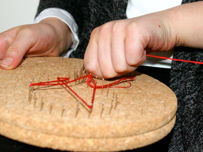 hands-crafting-a-diy-string-art-with-red-string-and-pins-on-a-cork