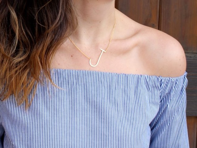 woman-wearing-a-blue-and-white-striped-off-the-shoulder-shirt-gold-j-necklace