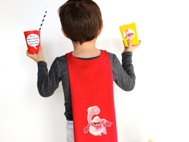boy-wearing-a-captain-underpants-cape-and-holding-a-yellow-popcorn-box-and-red-cup