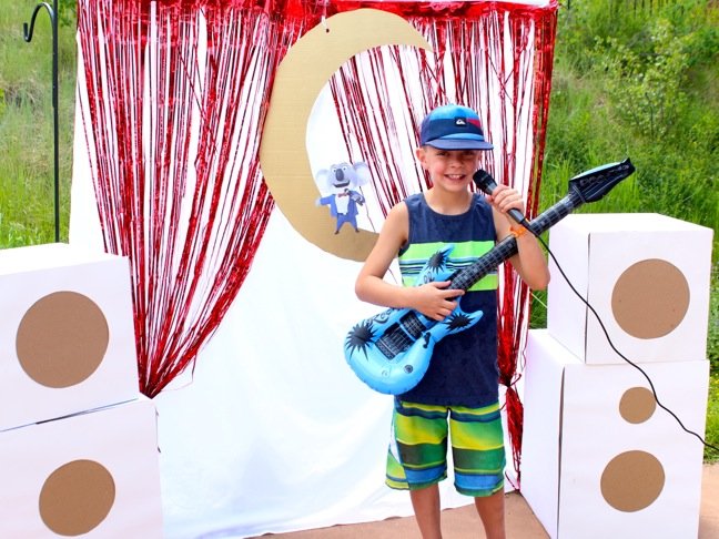 boy-wearing-a-hat-and-holding-a-guitar-siniging-on-a-microphone-with-a-diy-mini-stage