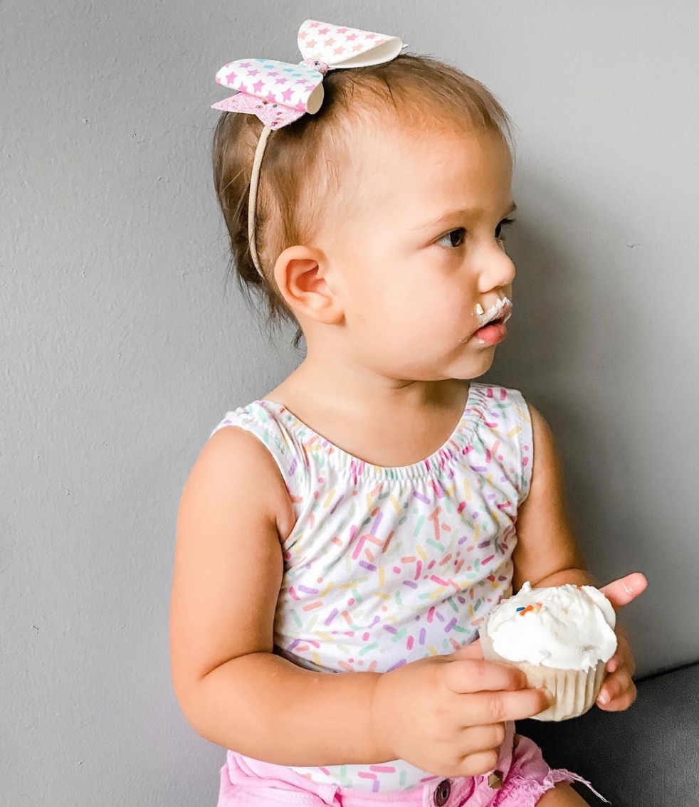 little-girl-in-big-bow-eating-rainbow-cupcake-with-vanilla-frosting