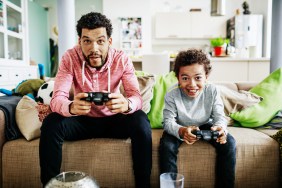 A father and son are concentrating while sitting down at home playing video games together.