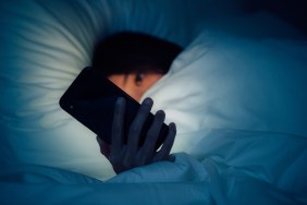 Woman hiding under the blanketed and using smart phone at late night on bed