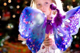 A three year old girl on Christmas morning in front of a Christmas tree with her new fairy doll. Background is filled with colorful Christmas tree lights.