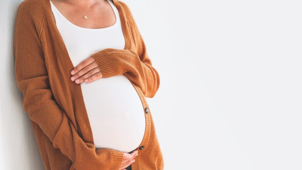 Beautiful pregnant woman touching her belly with hands on a white background.