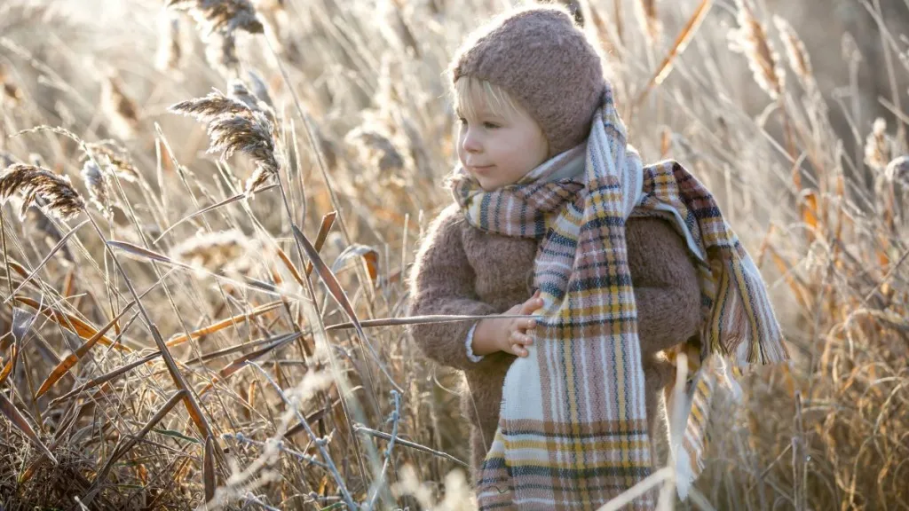 Beautiful toddler boy, dressed in knitted outfit with hat and flannel scarf, playing in frosty morning forest