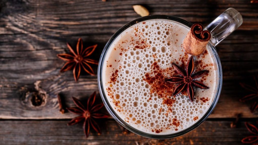 Homemade Hot Spiced Milk with anise and cinnamon stick in glass mug on wooden rustic background.