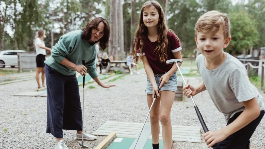 Siblings playing miniature golf with family in backyard