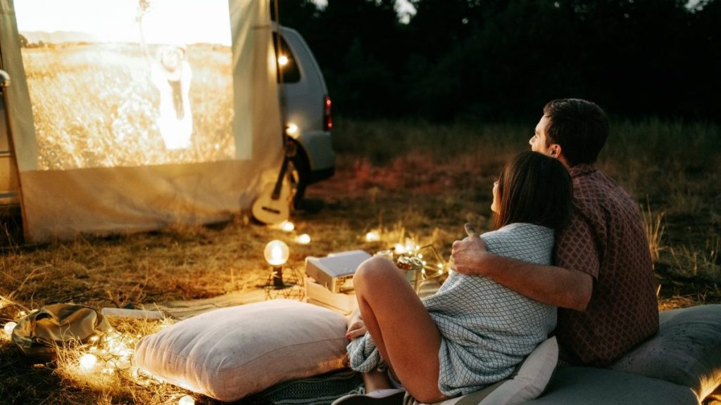 Young couple having movie night party. Laying down on blanket in front in the nature