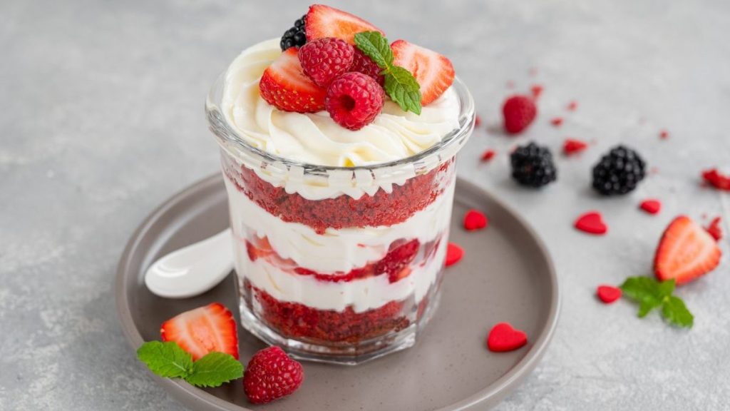 Red Velvet cake trifle with fresh berries in a glass jar on a gray concrete background. Dessert for Valentine's Day.