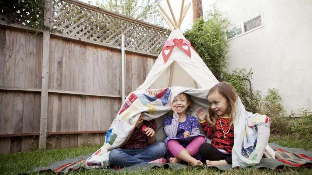 Three young girls in garden hiding under blanket in a teepee