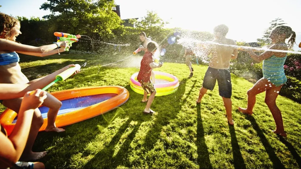 Group of young kids having water fight with squirt guns in backyard of home