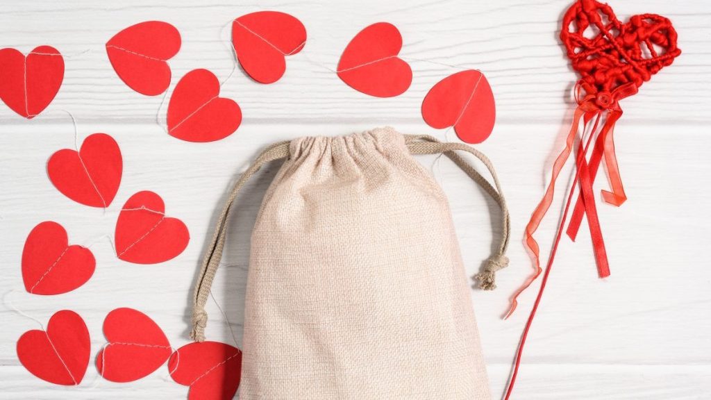 Mockup jute sack with paper red hearts. Valentines mockup white on white wooden background, flat lay, top view, copy space.