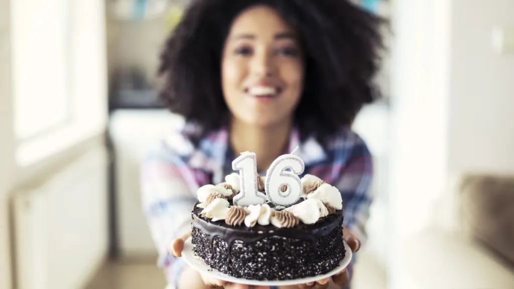 Smiling woman holding cake with candles for her 16th birthday.