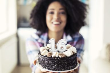 Smiling woman holding cake with candles for her 16th birthday.