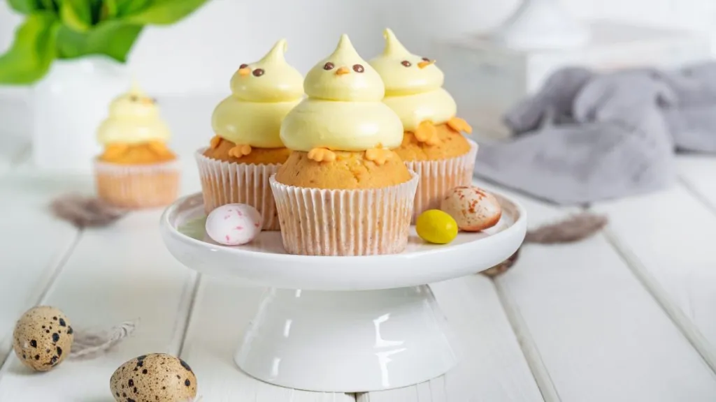 Cute Easter chick cupcakes. Vanilla cupcakes with buttercream on a white stand with fresh flowers