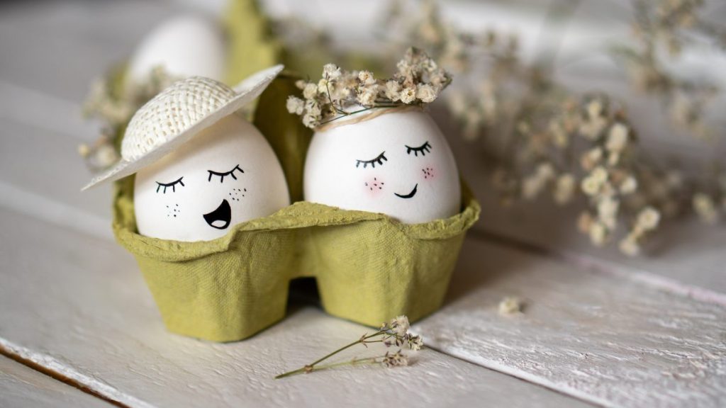 Minimalist Easter decoration on white Easter eggs. Eggs are smiley, beautiful and cute. They are placed in green egg container surrounded by small white dry flowers.