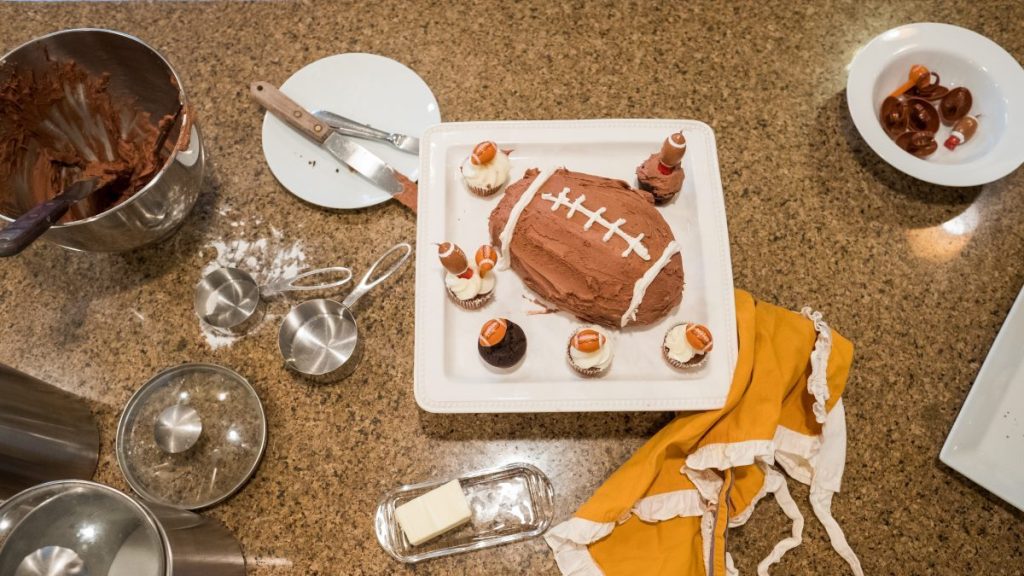 football shaped cake with plastic footballs on kitchen counter with cooking supplies