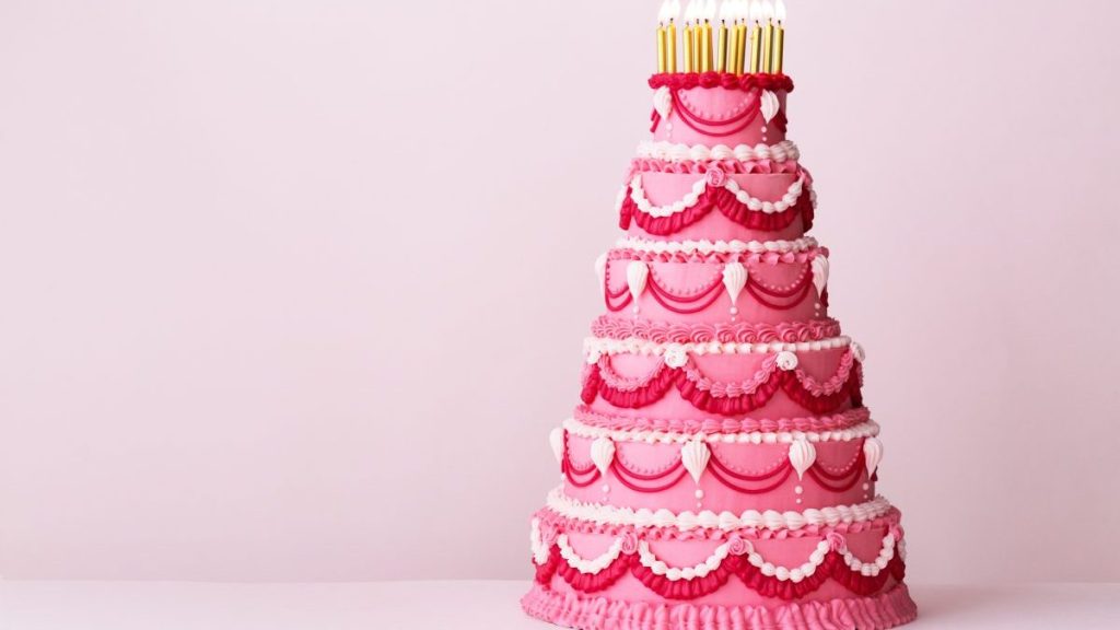 Extravagant pink tiered birthday cake decorated with vintage buttercream piped frills and gold birthday candles