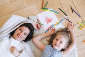 Preschool little girl with mother drawing on floor at bright room at home, view from top