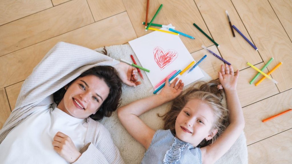 Preschool little girl with mother drawing on floor at bright room at home, view from top