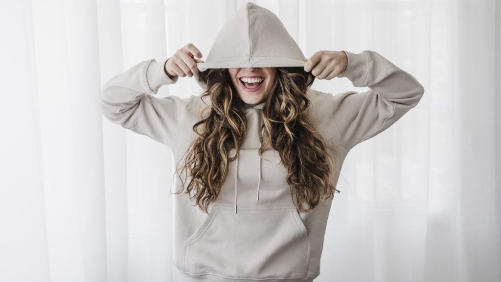 Playful woman covering eyes with hood at home