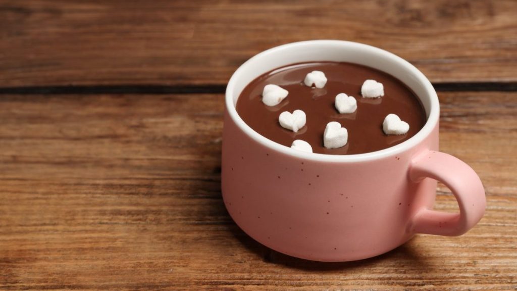 Cup of hot chocolate with heart shaped marshmallows on wooden table, space for text