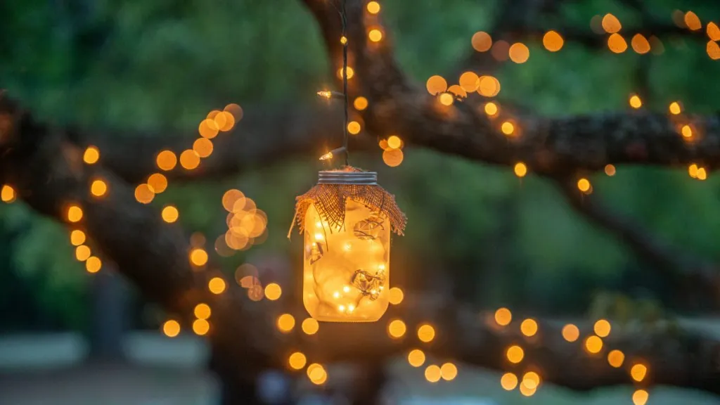 Mason jars filled with warm glowing lights decorations hanging from trees drapped in lights